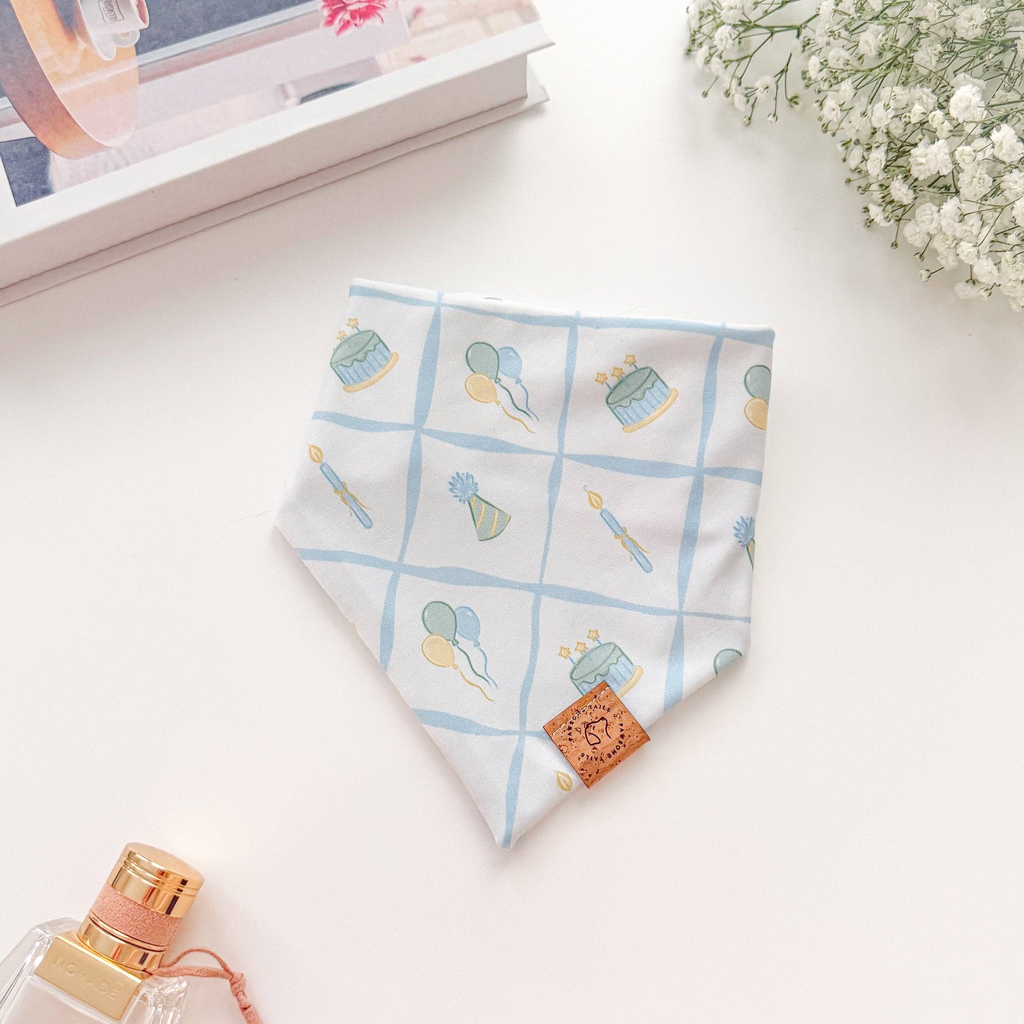Fabric with floral pattern on a white surface with a perfume bottle and flowers.