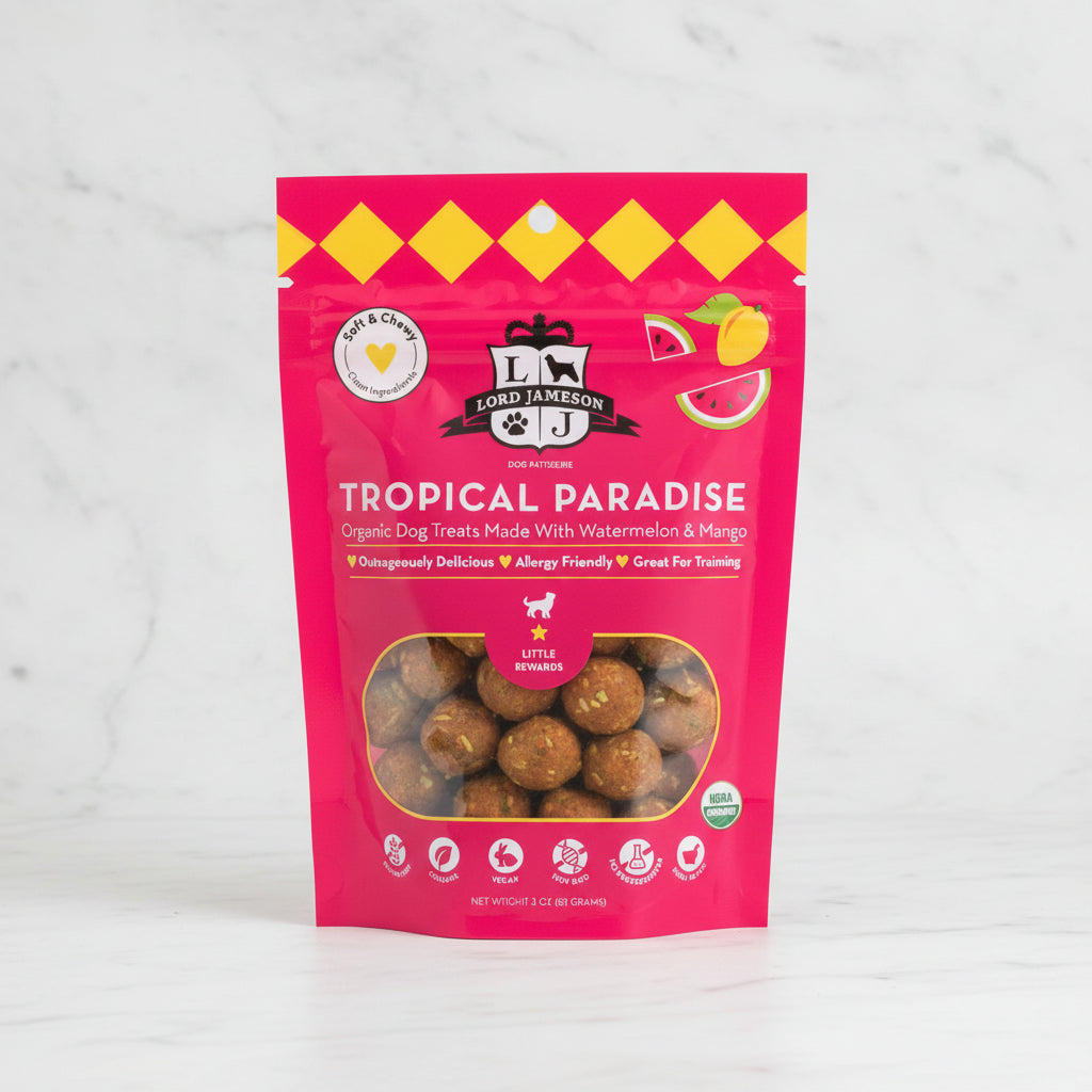 Pink package of 'Tropical Paradise' dog treats with watermelon and mango on a white background