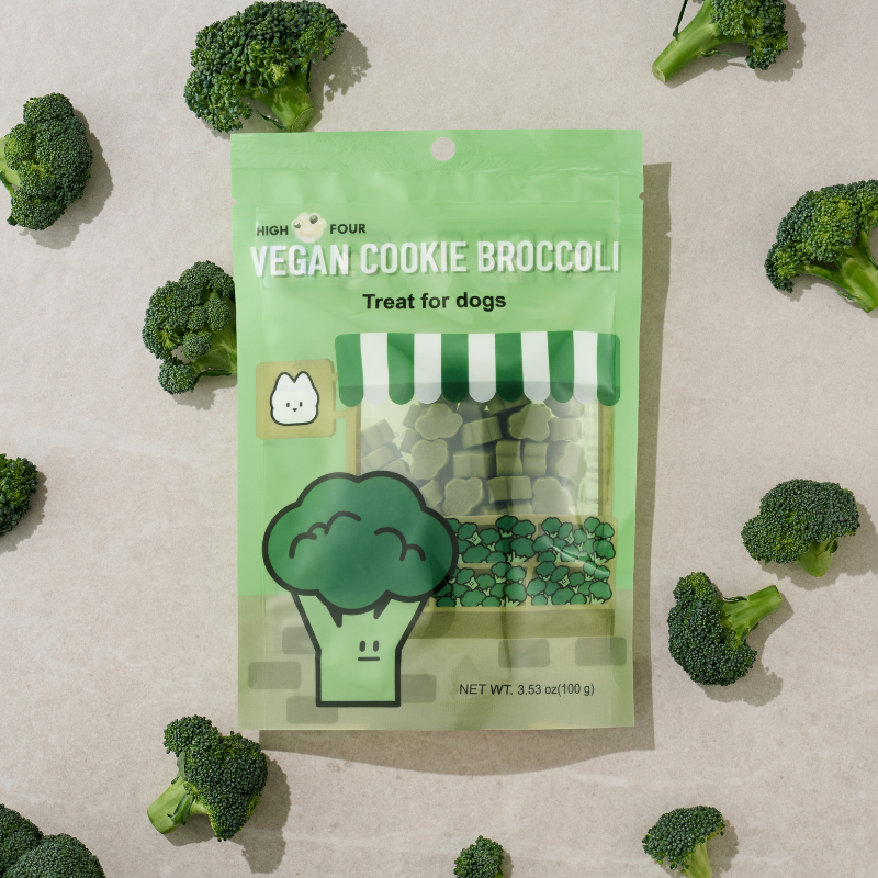Vegan cookie broccoli treat package surrounded by broccoli pieces on a beige background