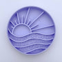 Round purple silicone mold with sun and wave design on a light purple background