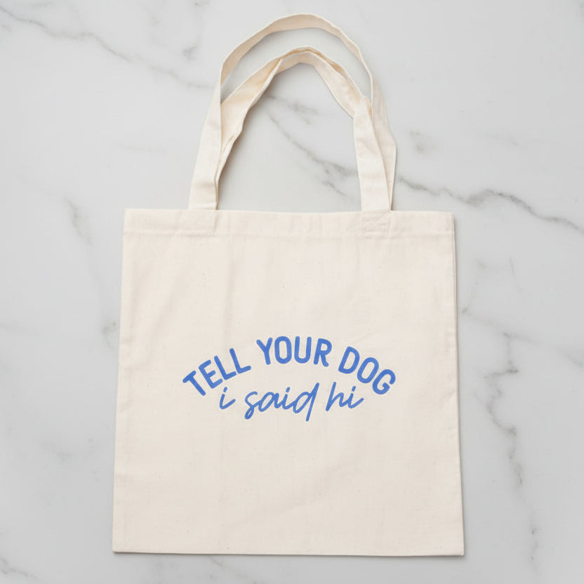 Beige tote bag with blue text 'Tell your dog I said hi' 