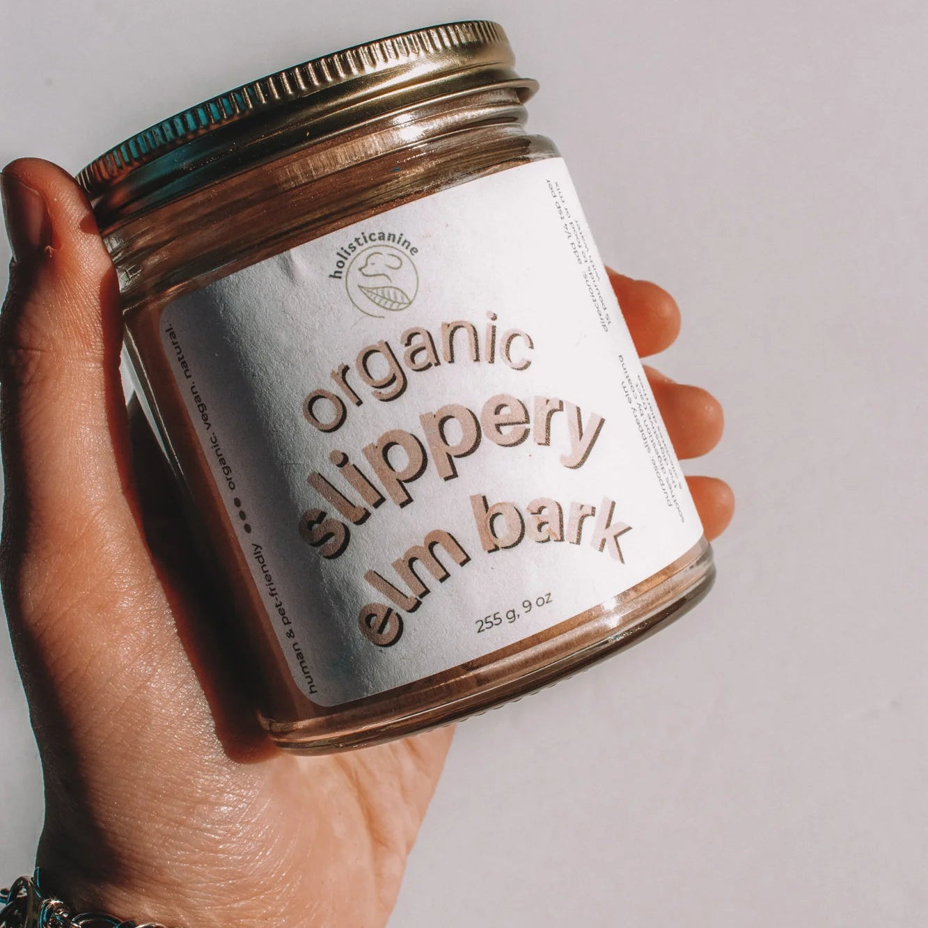 Hand holding a jar of organic slippery elm bark against a plain background